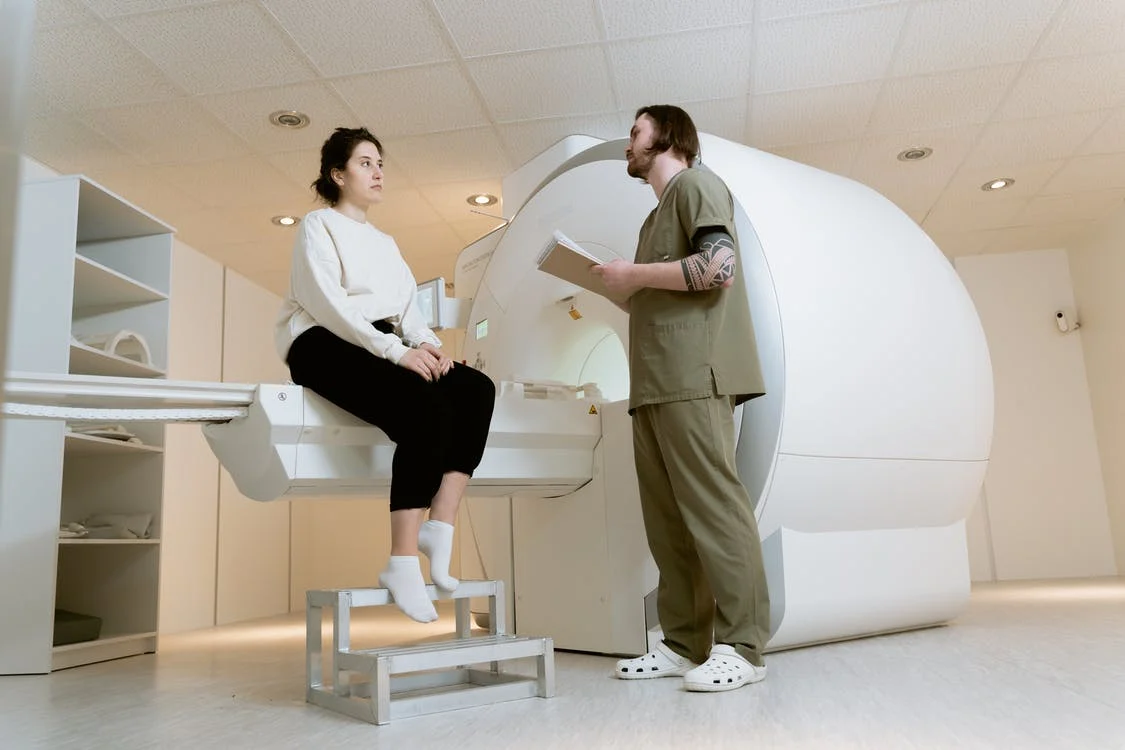 técnico em radiologia conversa com mulher sentada em maca de tomógrafo